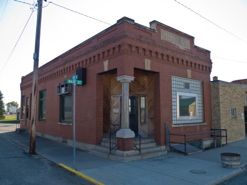 Historic brick bank building on a corner, featuring decorative elements and a ramp for accessibility.