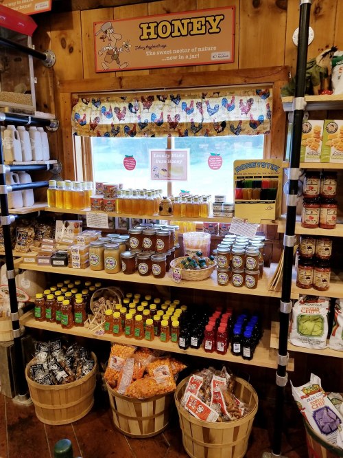 A wooden display featuring various jars of honey, snacks, and other local products in a rustic shop setting.