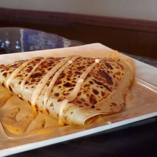A golden-brown crepe drizzled with sauce, served on a white plate with a glossy surface.