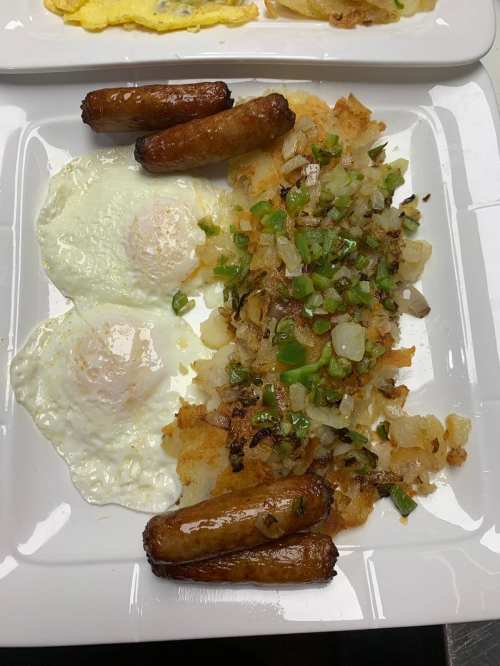 A plate of breakfast featuring two fried eggs, hash browns with green peppers and onions, and three sausage links.