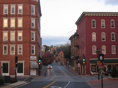 A quiet street scene with brick buildings, traffic lights, and a hint of autumn foliage in the background.