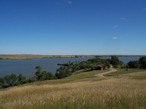 A serene landscape featuring a winding path, a lake, and lush greenery under a clear blue sky.