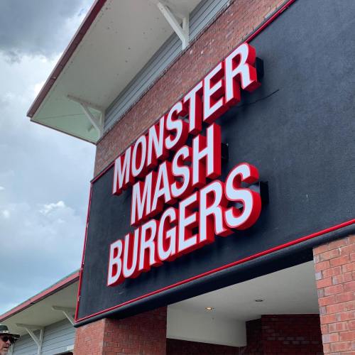 Sign for "Monster Mash Burgers" on a brick building with a cloudy sky in the background.
