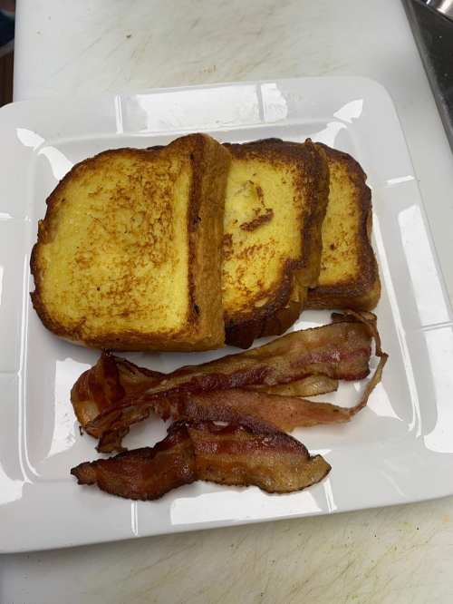 A plate with three slices of golden-brown French toast and crispy bacon strips.