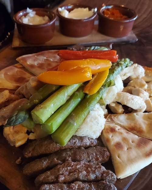 A colorful platter featuring grilled vegetables, meats, and pita bread, accompanied by small bowls of sauces.