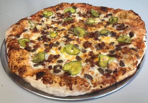 A large pizza topped with cheese, ground beef, and sliced pickles on a golden crust.