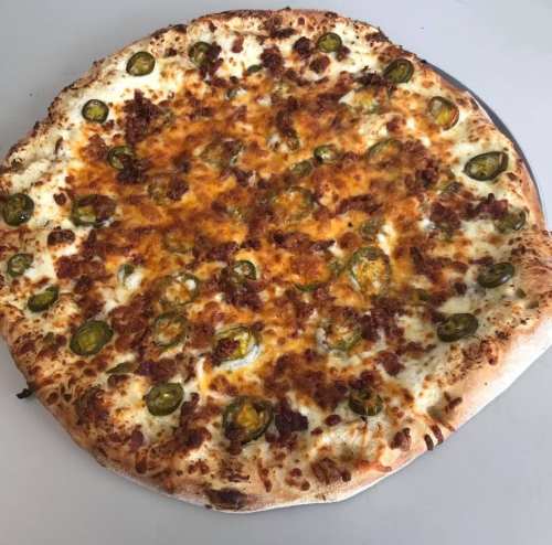 A large pizza topped with melted cheese, jalapeños, and crumbled meat on a golden crust.