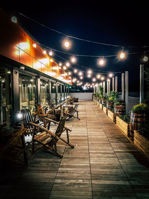 A wooden deck at night with string lights, chairs, and planters, creating a cozy outdoor atmosphere.