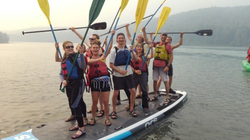 A group of people on a paddleboard, smiling and holding paddles, enjoying a day on the water.