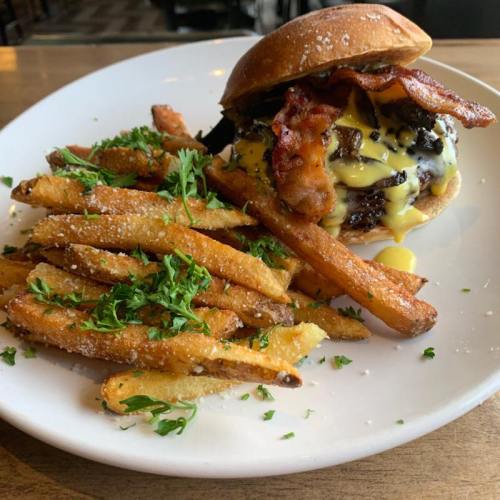 A juicy burger topped with bacon and cheese, served with crispy fries garnished with parsley on a white plate.