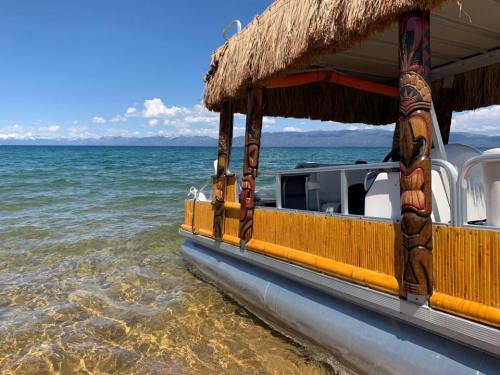 A tiki-style boat anchored in clear water, with mountains and a blue sky in the background.