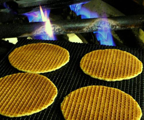 Four round waffles cooking over blue flames on a grill.