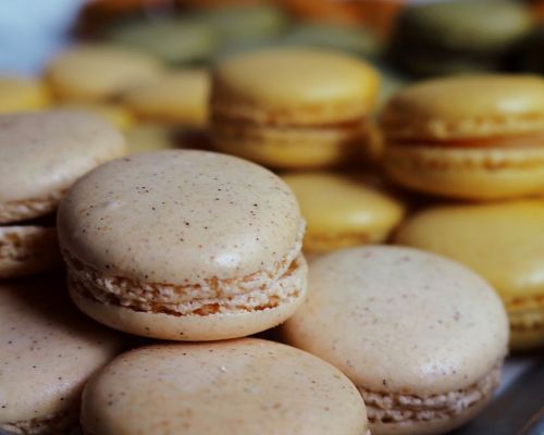 A close-up of golden macarons stacked together, with more macarons blurred in the background.