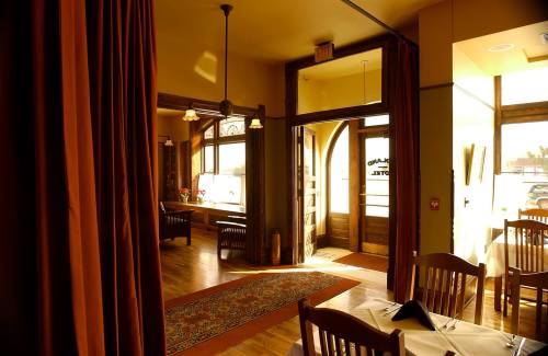 Interior of a restaurant with wooden furniture, warm lighting, and a welcoming entrance. Curtains frame the view.