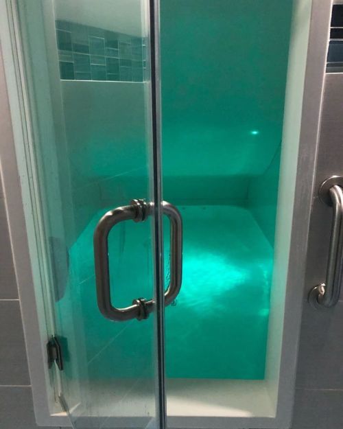 A modern shower with a glass door, featuring turquoise water and ambient lighting inside.