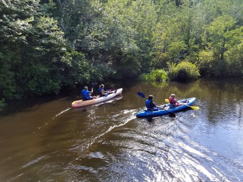 Two people kayak on a calm river surrounded by lush greenery, with one person in a canoe nearby.