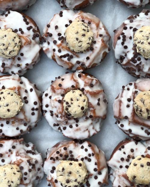 A close-up of chocolate frosted donuts topped with cookie pieces and mini chocolate chips on a white background.
