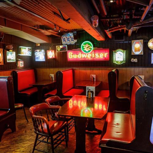 Cozy bar interior with red booths, wooden tables, and colorful beer signs on the walls.