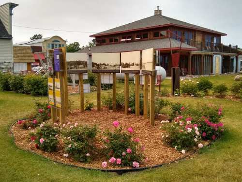 A landscaped area with flower beds and informational signs in front of a modern building.