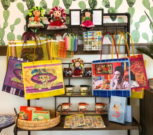 Colorful display of bags, dolls, and pottery on a shelf, with a cactus-themed background.