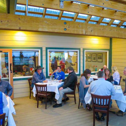 A cozy restaurant scene with diners at tables, warm lighting, and a wooden ceiling, creating an inviting atmosphere.