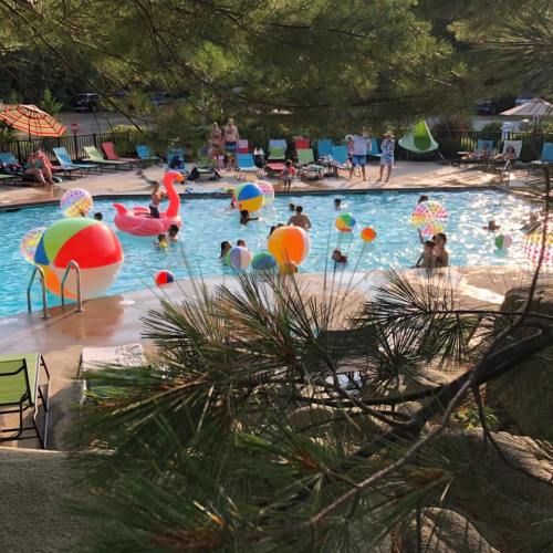 A lively pool scene with people swimming and playing with colorful beach balls and floats on a sunny day.