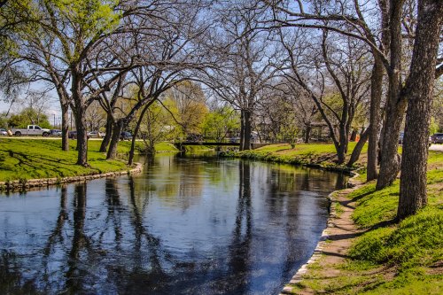 A serene river scene with trees lining the banks and a clear blue sky reflecting on the water's surface.