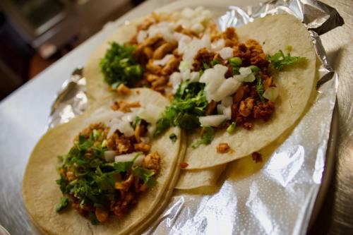 Three tacos on a silver tray, filled with chopped meat, onions, and cilantro.