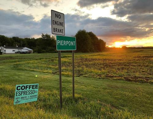 A sunset over a field with signs for "No Engine Brake" and "Pierpont," alongside a coffee shop advertisement.