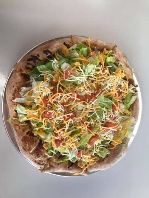 A large pizza topped with lettuce, tomatoes, cheese, and tortilla chips on a whole wheat crust.