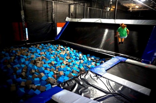 A person jumps on a trampoline near a large pit filled with blue and gray foam blocks.