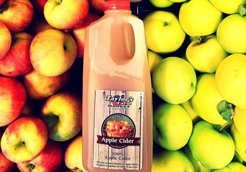 A bottle of apple cider surrounded by red and green apples at a market.