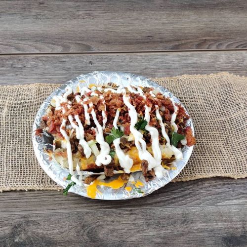 A silver plate filled with loaded nachos topped with bacon, cheese, sour cream, and fresh herbs on a rustic table.