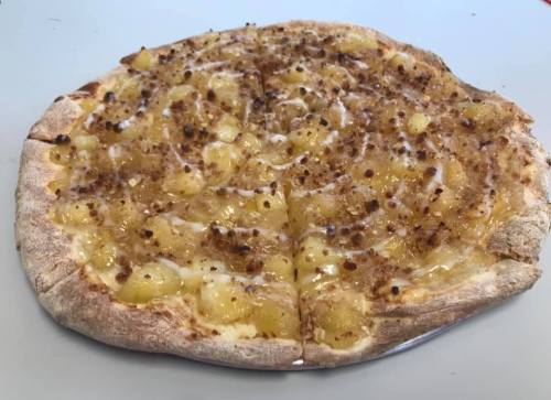 A pizza topped with pineapple, cheese, and a sprinkle of crumbled topping on a golden-brown crust.