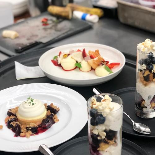 Three elegant desserts on black plates: a layered parfait with blueberries, a creamy tart, and a fruit plate with strawberries.