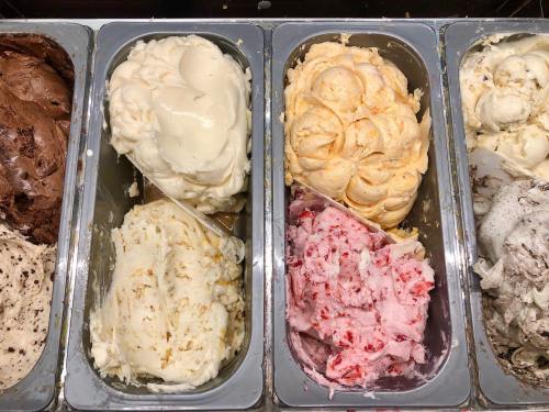 A variety of ice cream flavors in metal containers, including chocolate, vanilla, orange, and strawberry.