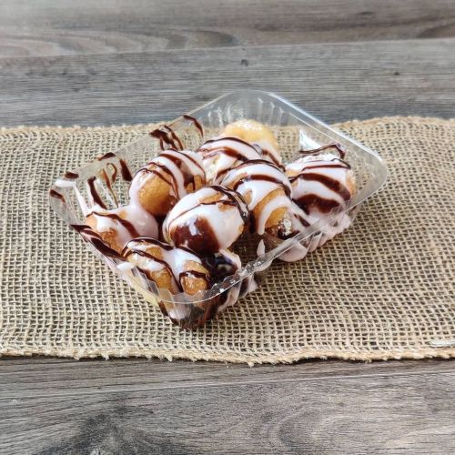 A clear container filled with round pastries drizzled with chocolate and white icing, placed on a textured surface.