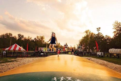 A child jumps joyfully on a large inflatable bounce pad at sunset, with a festive atmosphere in the background.