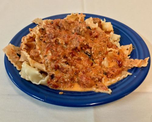 A blue plate filled with pasta topped with a creamy, meat sauce and herbs.
