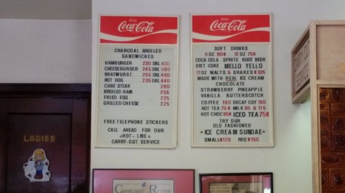 Menu board featuring sandwiches and soft drinks with prices, including hamburgers, cheeseburgers, and ice cream options.