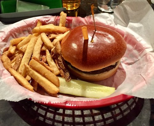 A burger with a pickle and a toothpick, served with a side of golden fries in a red basket.