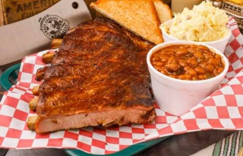 A plate of BBQ ribs with toast, coleslaw, and baked beans, served on a checkered paper.