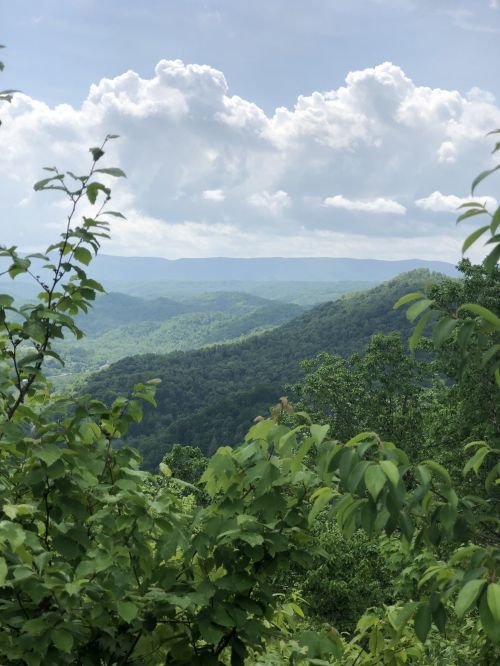 Lush green mountains under a cloudy sky, with a panoramic view of rolling hills in the distance.