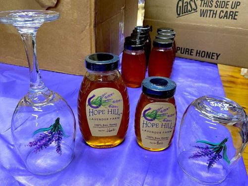 A table with a wine glass and jars of Hope Hill Lavender Farm honey, surrounded by cardboard boxes.
