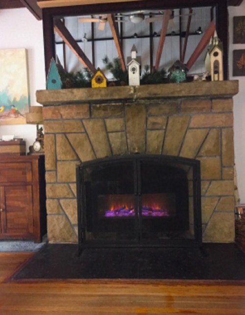 A cozy stone fireplace with a glass front, surrounded by decorative birdhouses and greenery on the mantel.