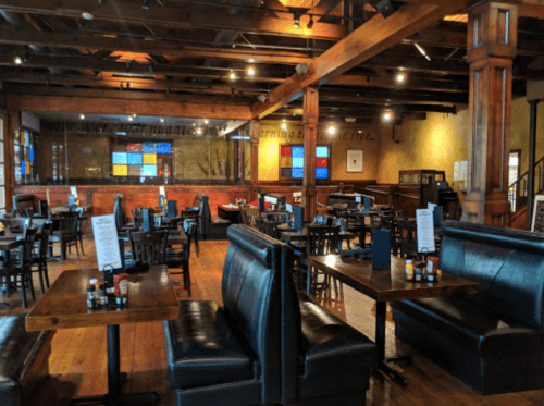 Interior of a restaurant featuring wooden beams, booths, and colorful stained glass windows. Tables are set for dining.