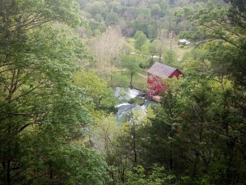 A red barn by a river, surrounded by lush green trees and a peaceful landscape.