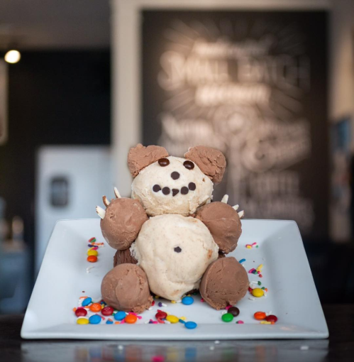 A playful ice cream creation shaped like a bear, topped with chocolate and colorful sprinkles on a white plate.