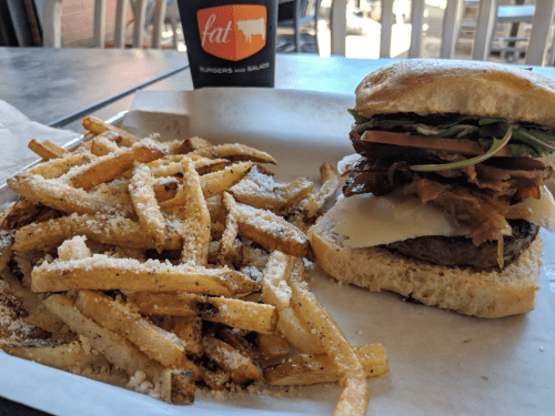 A plate with a burger topped with lettuce, tomato, and bacon, alongside a serving of seasoned fries and a drink.
