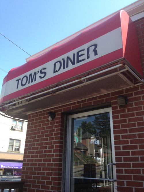 A red and white awning with the text "Tom's Diner" above a brick building entrance.